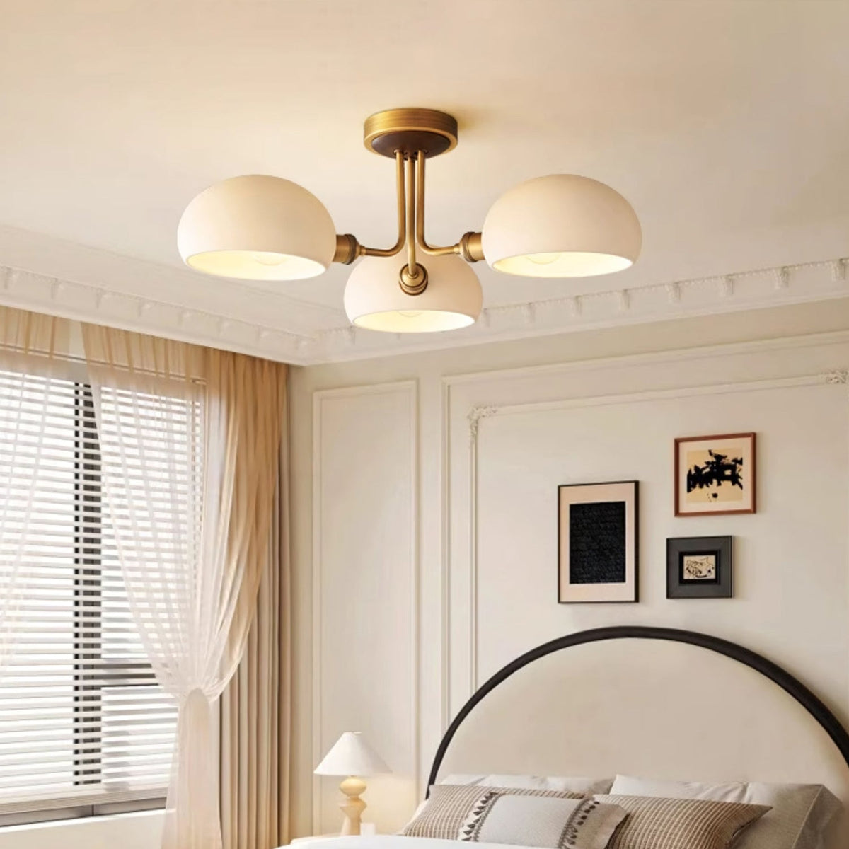 This Clérachic ceiling light glows warmly above a cream-panelled bedroom with a black arched headboard and sheer curtains.