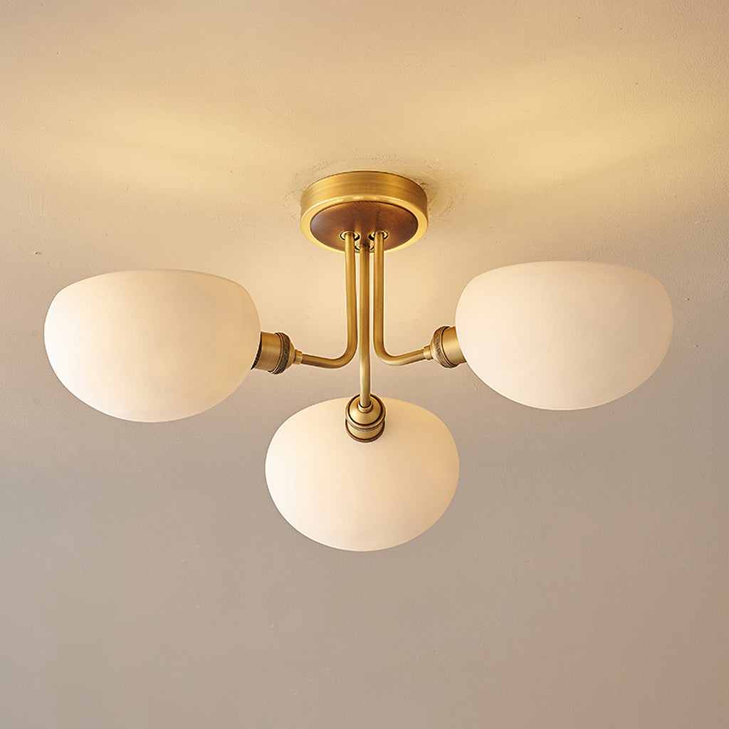 Close view from below of the brass stem and three rounded white shades on this Clérachic ceiling light, lit warm.