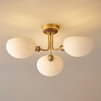 Close view from below of the brass stem and three rounded white shades on this Clérachic ceiling light, lit warm.
