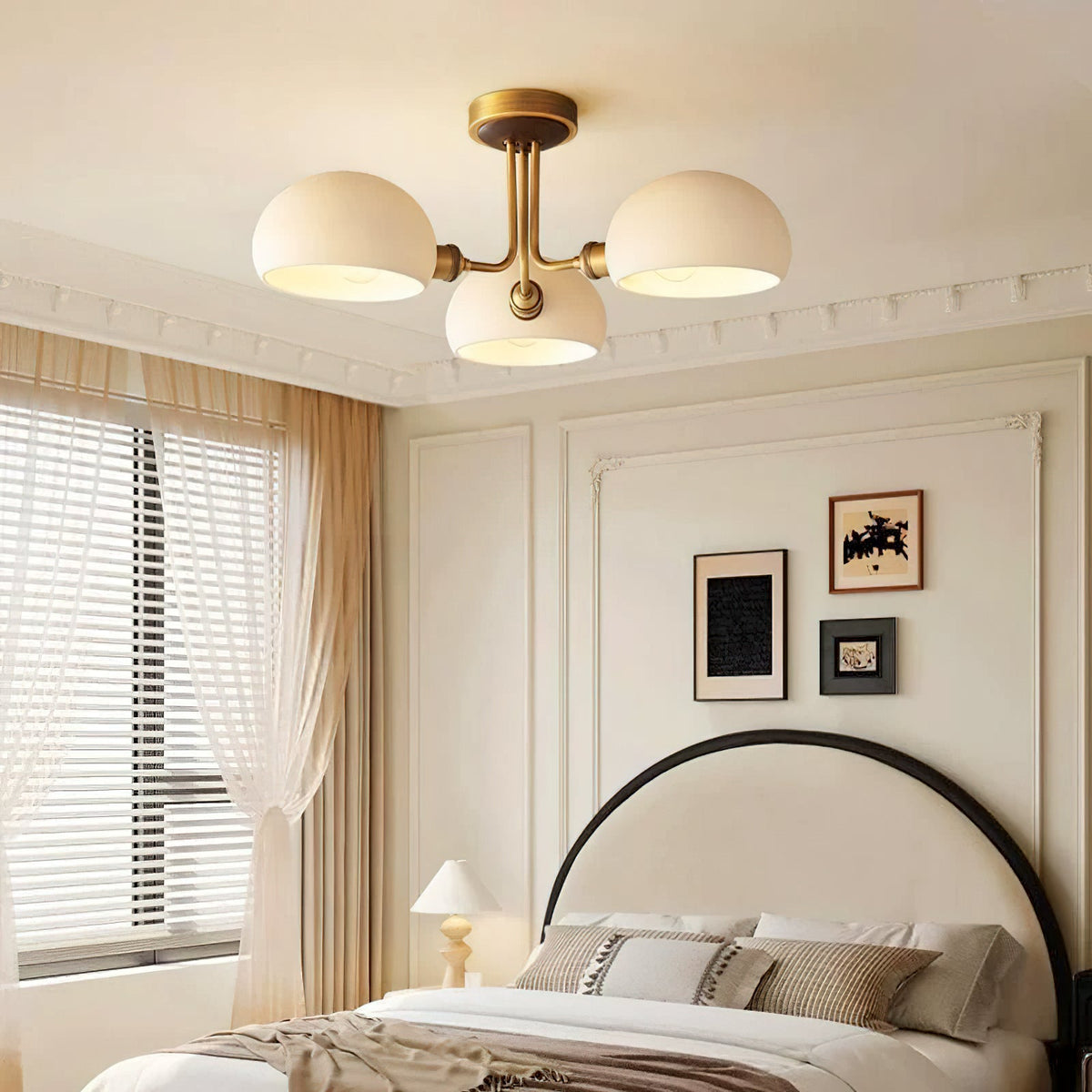 Wide bedroom view with a Clérachic three-light ceiling light switched on over a cream bed, striped curtains and framed prints.
