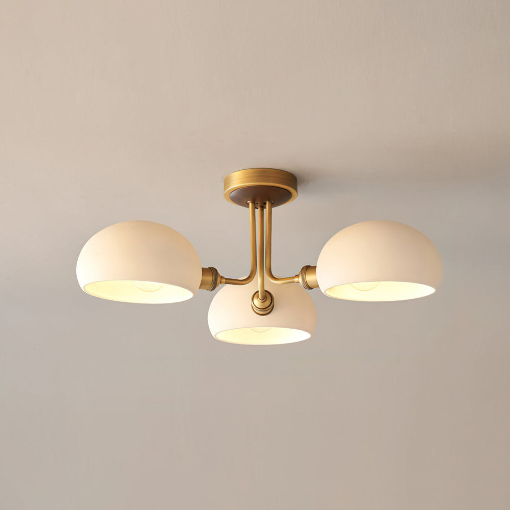 Three white globe shades with a warm glow inside, on a brass fixture from Clérachic against a beige ceiling.