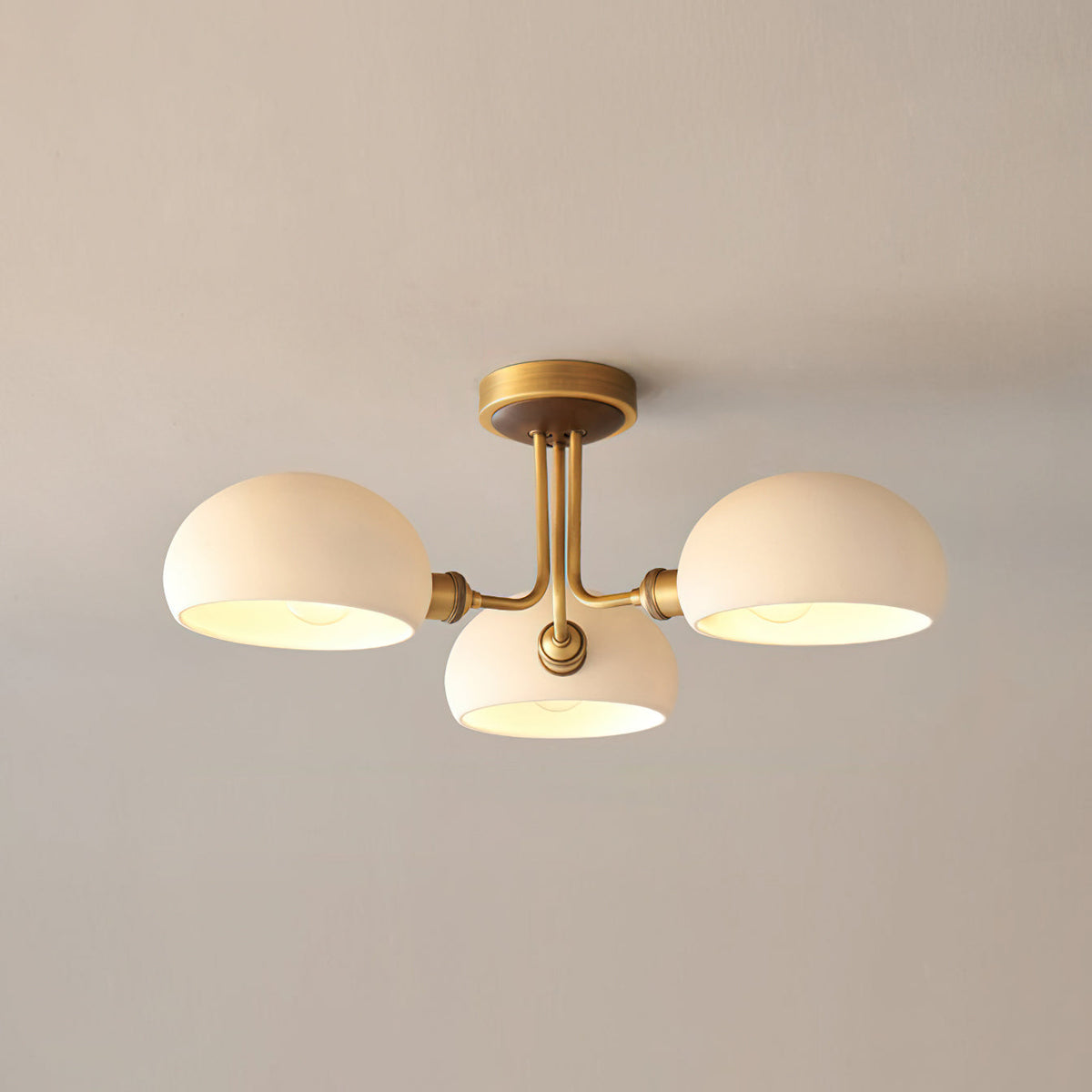 Three white globe shades with a warm glow inside, on a brass fixture from Clérachic against a beige ceiling.