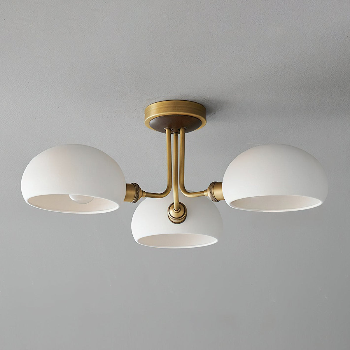 Unlit brass and white ceramic ceiling light from Clérachic against a pale grey ceiling, the shades open downward.