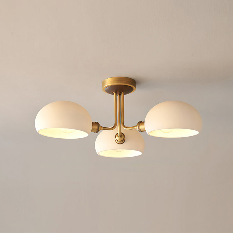 Front view of this Clérachic brass ceiling light, its three white shades lit from inside against a soft beige wall.