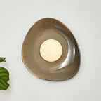 Close view of a Clérachic pebble-shaped wall light, its glossy taupe glaze curving around a round white globe.