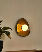 A Clérachic ceramic wall light glowing warm on a beige wall, its round globe lit and the glossy glaze catching the light.