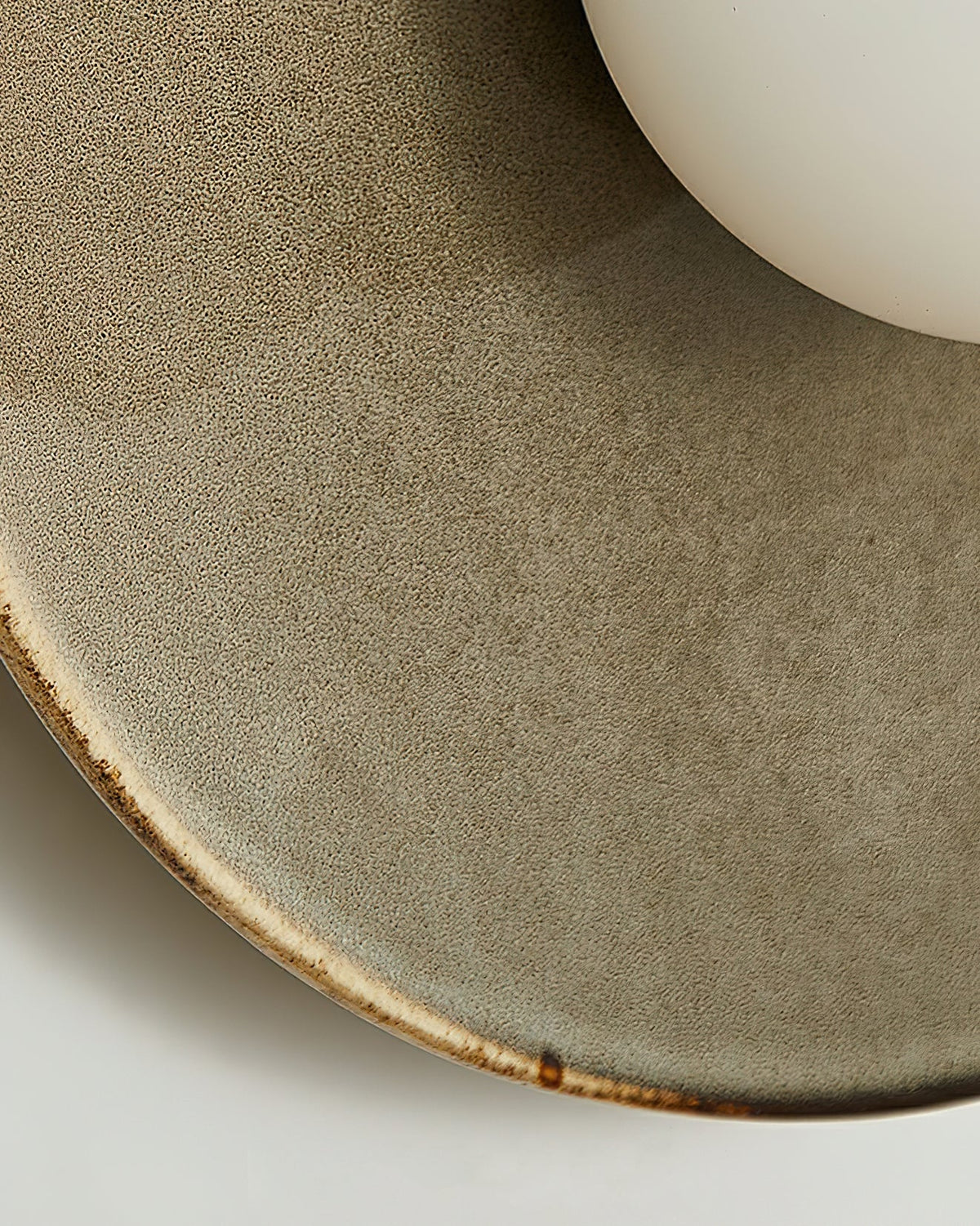 Close view of the speckled taupe glaze and the brown-edged rim on this Clérachic ceramic wall light, beside the white globe.
