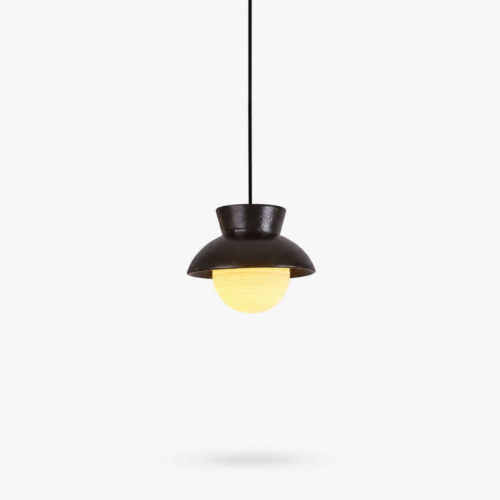A black ceramic Clérachic pendant with a flared hood and a ribbed, softly lit glass globe below, on a plain white backdrop.