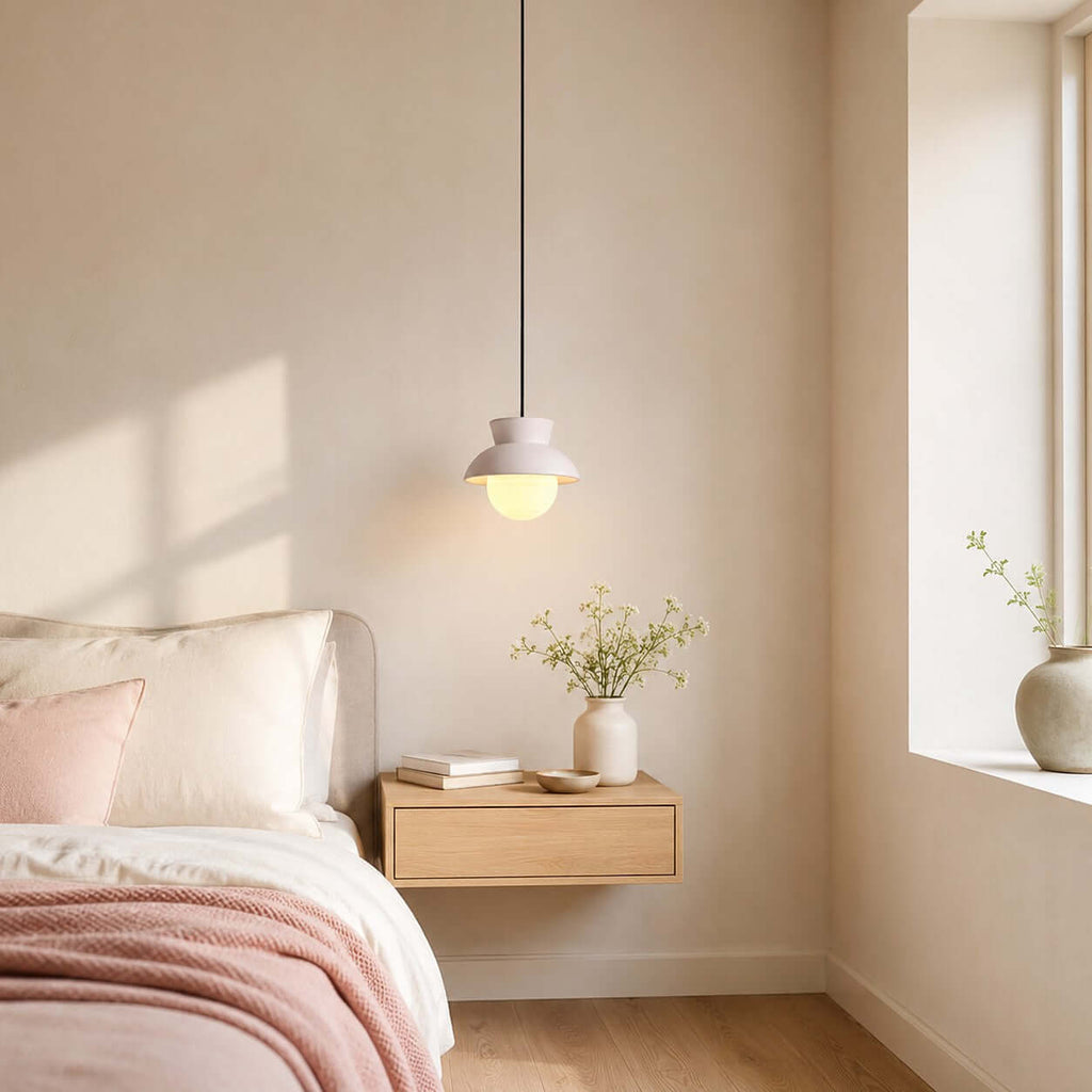 Sunlight falls across a bedroom where a small Clérachic pendant with a pale blush hood hangs above a floating oak bedside shelf.