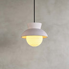 Close view of a Clérachic pendant with a pale blush hood and a lit, finely ribbed glass globe, on a grey plaster wall.