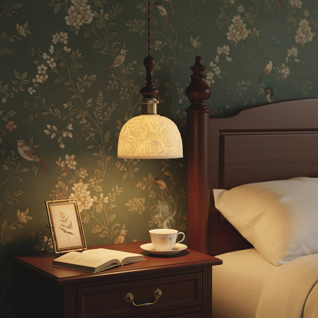 This Clérachic pendant glows beside a bed with a dark wooden headboard, against green floral wallpaper, above a cup of tea.