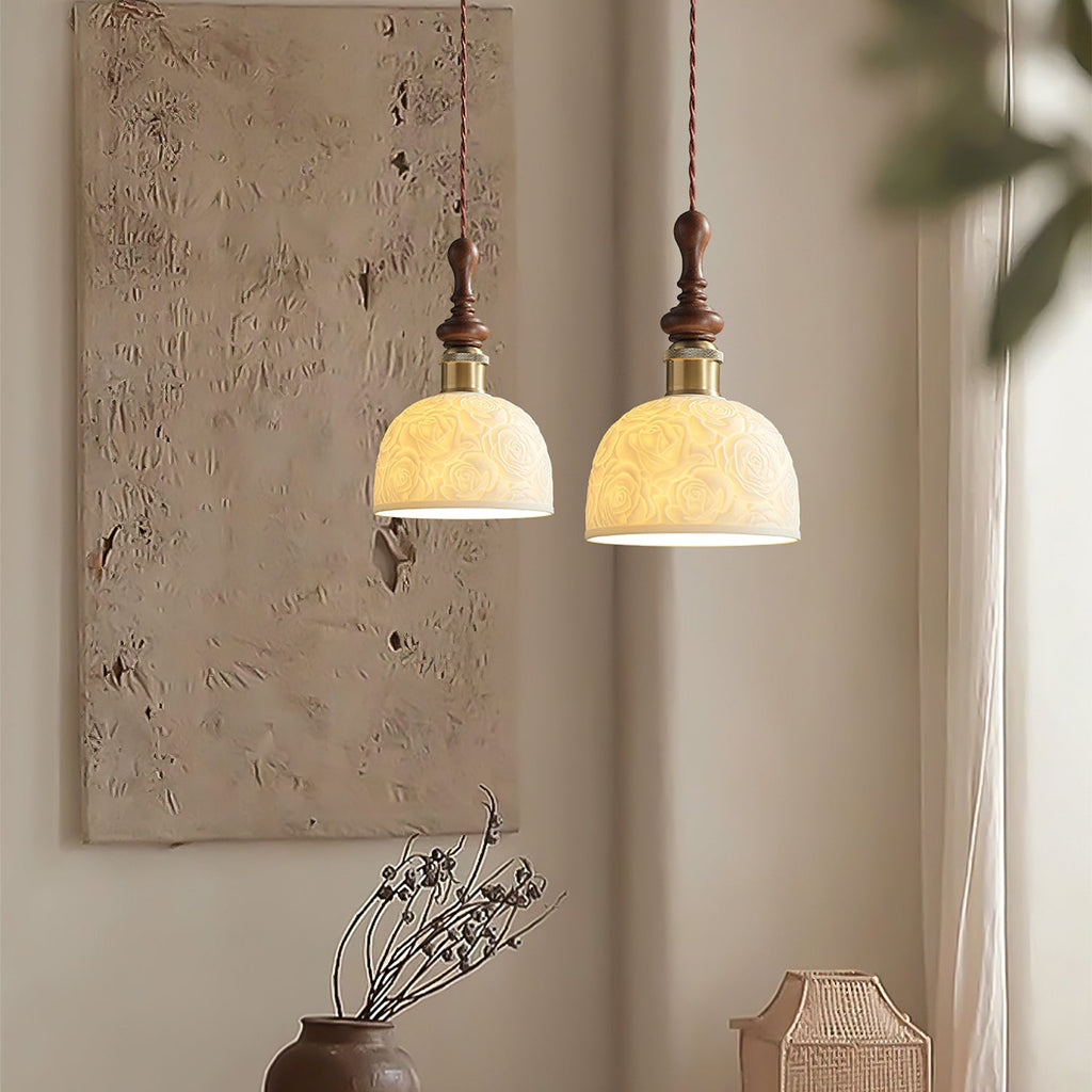 Two Clérachic pendants with rose-pattern ceramic shades lit side by side, in front of a textured wall panel.