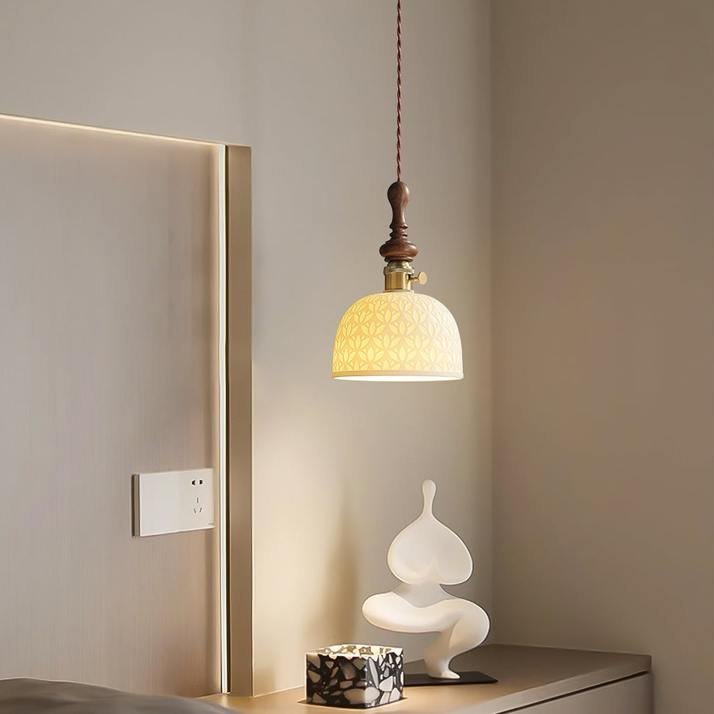 A rose-pattern ceramic Clérachic pendant lit above a pale sculptural ornament, beside a wall switch in a cream hallway.
