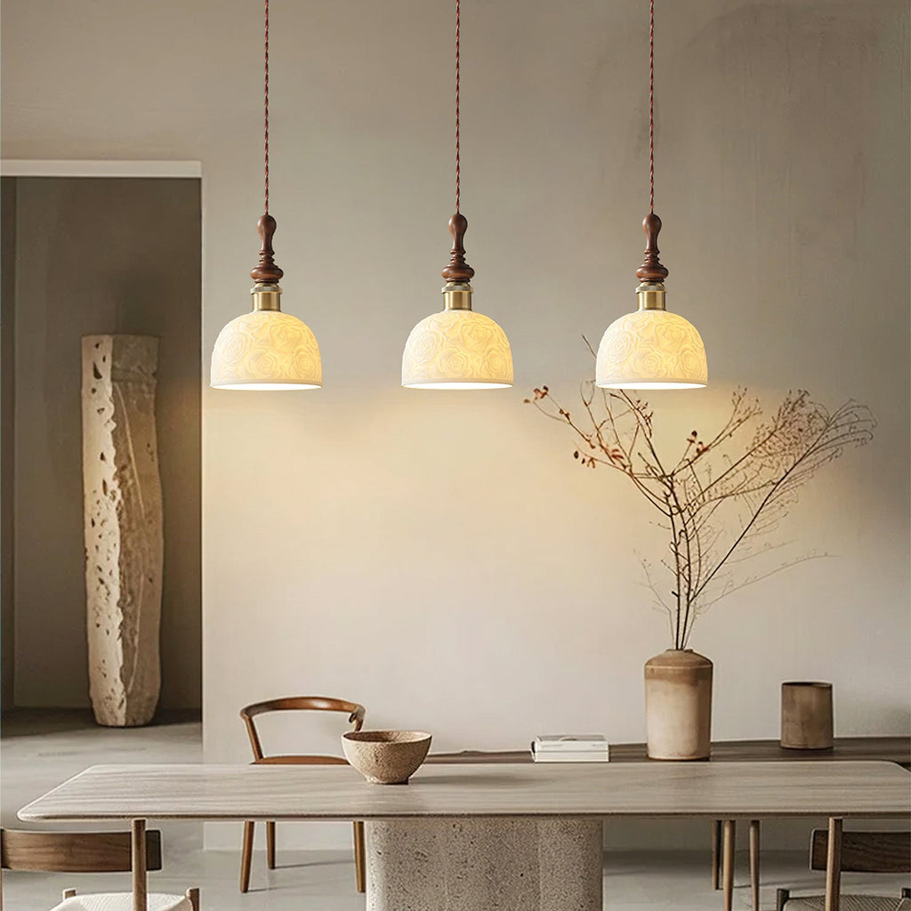 Three rose-pattern ceramic Clérachic pendants glowing above a stone dining table, with a vase of dry branches nearby.