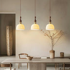Three rose-pattern ceramic Clérachic pendants glowing above a stone dining table, with a vase of dry branches nearby.