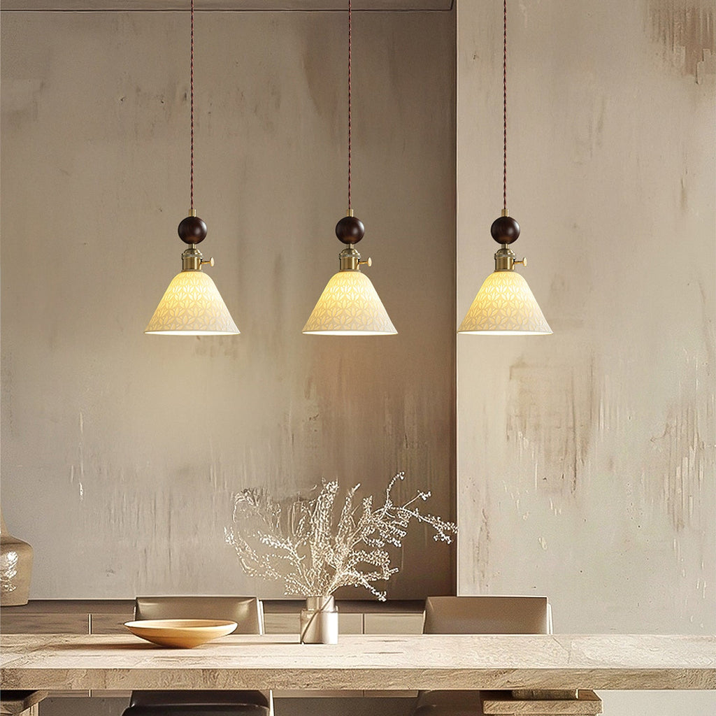 Three small flared ceramic Clérachic pendants with round walnut tops, lit above a pale wooden table and a shallow bowl.