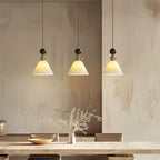 Three small flared ceramic Clérachic pendants with round walnut tops, lit above a pale wooden table and a shallow bowl.