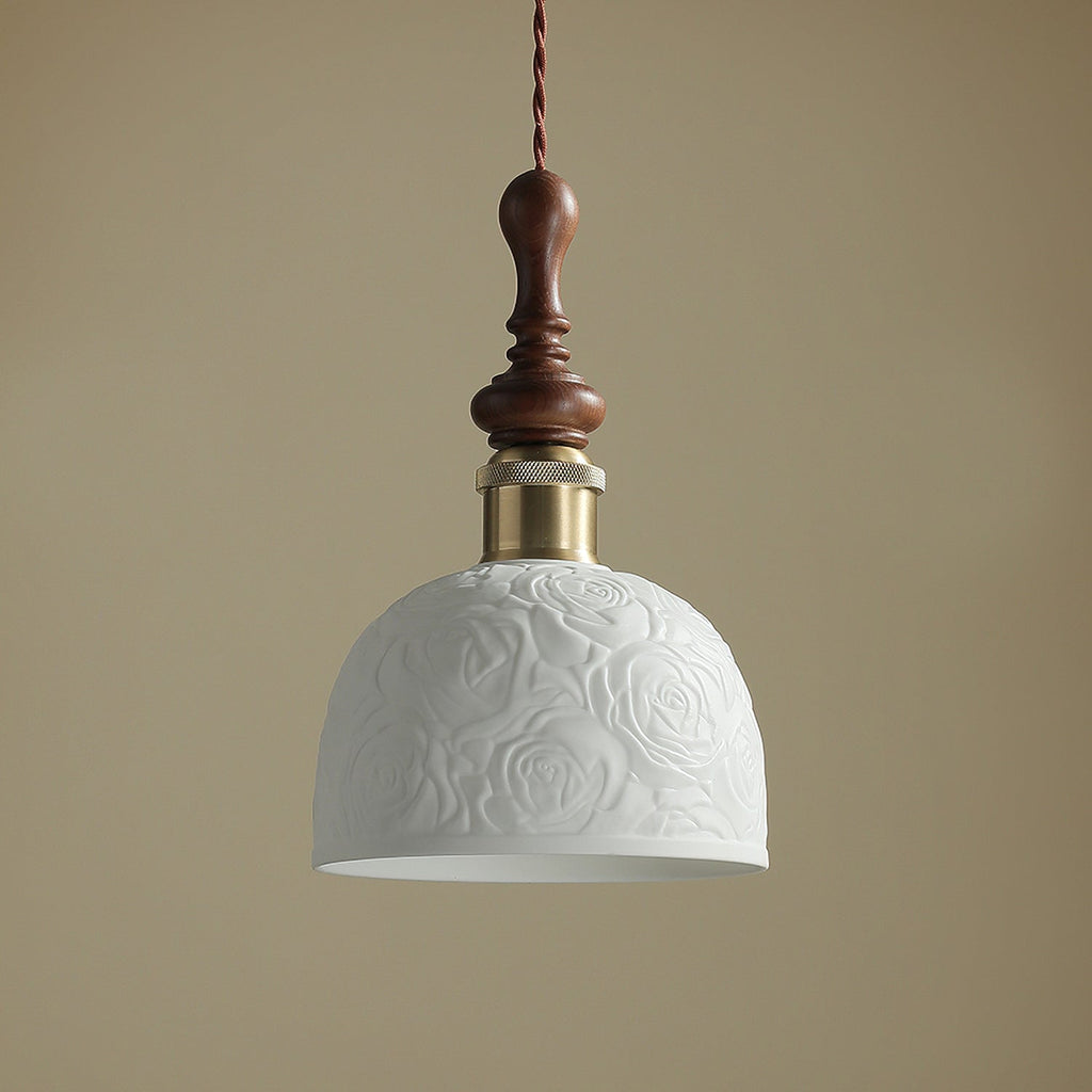 Close view of the rose pattern on the white ceramic shade of this Clérachic pendant, with its brass collar and turned walnut top.