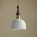 Close view of the rose pattern on the white ceramic shade of this Clérachic pendant, with its brass collar and turned walnut top.