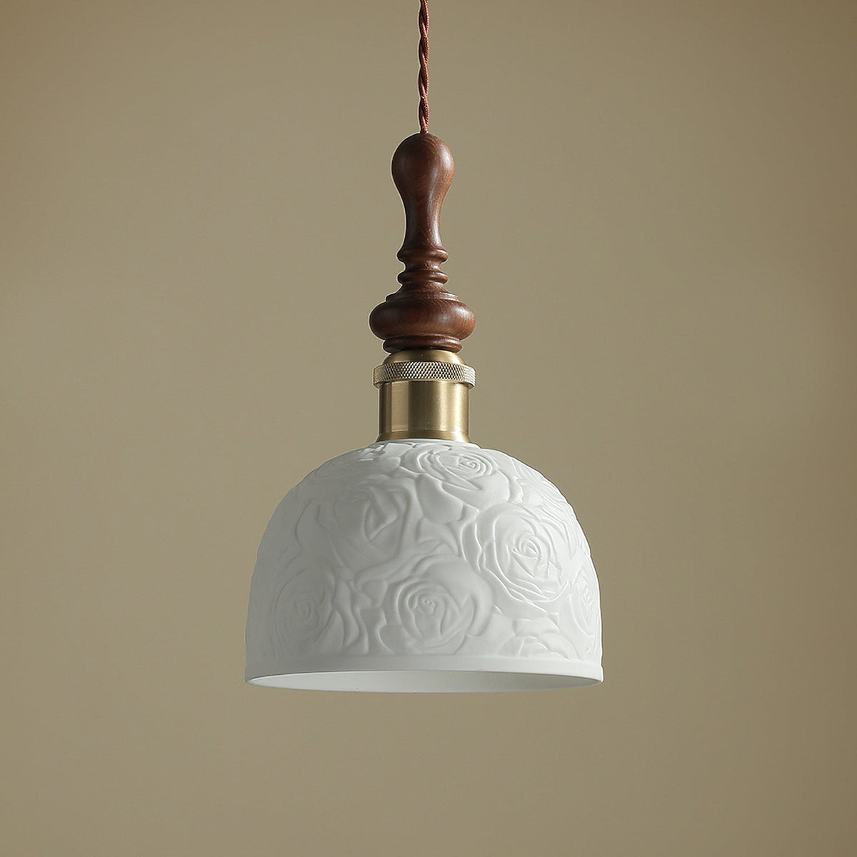 Close view of the rose pattern on the white ceramic shade of this Clérachic pendant, with its brass collar and turned walnut top.
