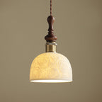 This Clérachic pendant lit, with warm light showing through the rose-pattern ceramic shade, against a tan wall.