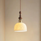 A rose-pattern ceramic Clérachic pendant lit, with a turned walnut top and a brass-coloured collar, against a warm beige wall.
