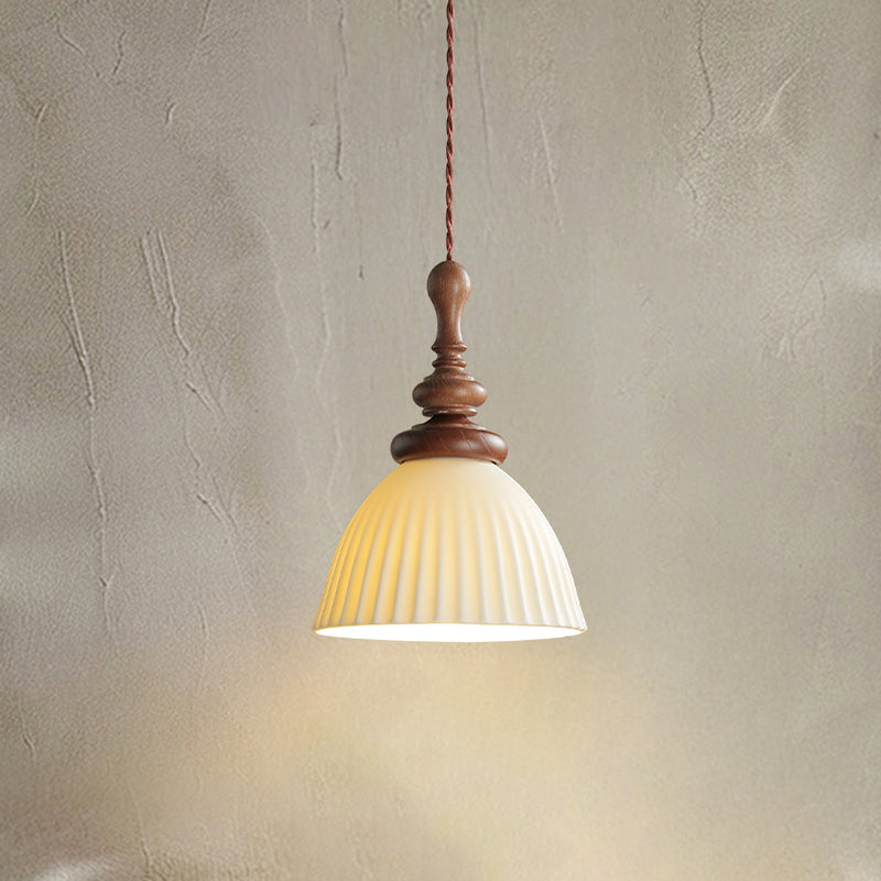 A tall ribbed ceramic Clérachic pendant lit, with a turned walnut top and a twisted red-and-cream cord, on a plaster wall.
