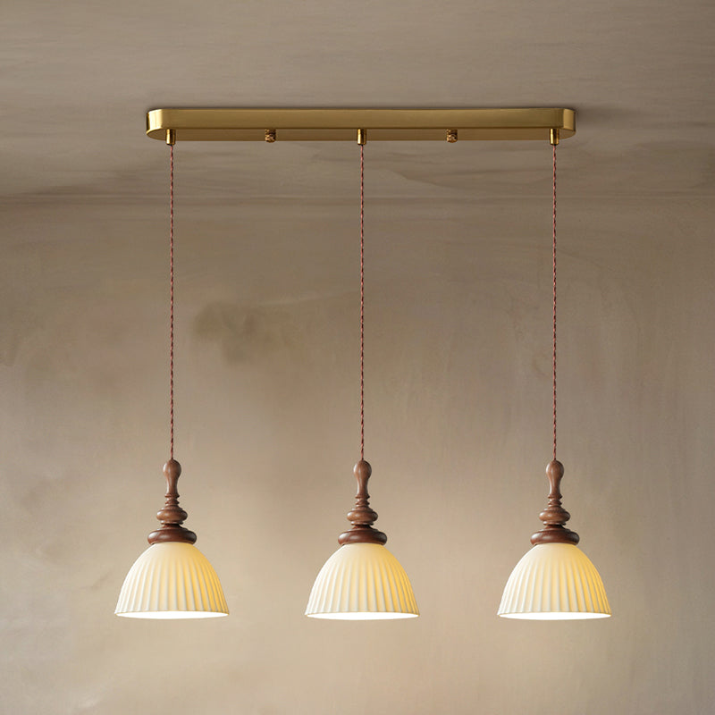 Three ribbed ceramic Clérachic pendants hung from a brass bar canopy, on twisted cords, against a warm plaster wall.
