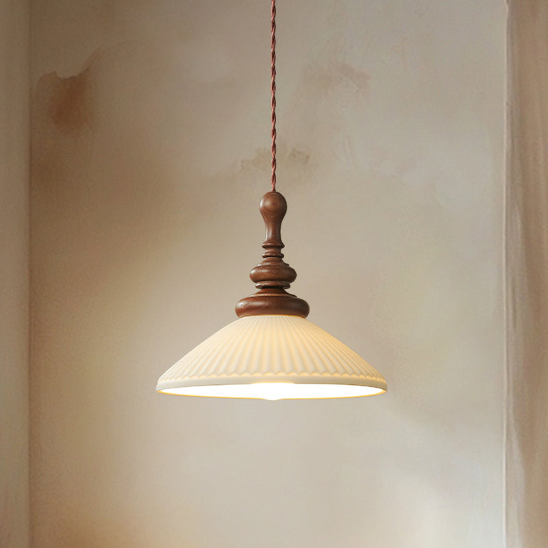 A wide, flared ribbed ceramic Clérachic pendant lit, with a turned walnut top, against a soft plaster wall.
