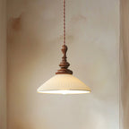 A wide, flared ribbed ceramic Clérachic pendant lit, with a turned walnut top, against a soft plaster wall.