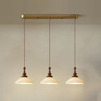 Three flared ribbed ceramic Clérachic pendants lit and hung from a long brass bar canopy against a pale wall.