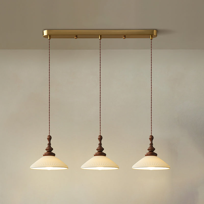 Three flared ribbed ceramic Clérachic pendants lit and hung from a long brass bar canopy against a pale wall.