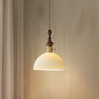 A dome-shaped ribbed ceramic Clérachic pendant lit, with a brass switch collar and a turned walnut top, against a curtain.