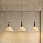 Three small ribbed ceramic Clérachic pendants lit in a row, hung on twisted cords against a rough plaster wall.