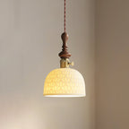 A dome-shaped ceramic Clérachic pendant with a pierced star pattern, lit, with a brass switch collar and walnut top.