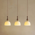 Three dome-shaped Clérachic pendants with a pierced star pattern, lit and hung on twisted cords against a plaster wall.