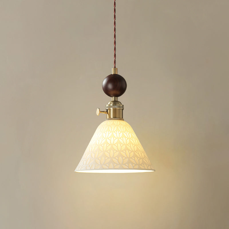 A cone-shaped ceramic Clérachic pendant with a pierced star pattern, lit, under a round walnut ball and brass switch collar.