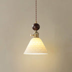 A cone-shaped ceramic Clérachic pendant with a pierced star pattern, lit, under a round walnut ball and brass switch collar.