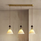 Three cone-shaped ceramic Clérachic pendants with round walnut tops, lit and hung from a brass bar canopy.