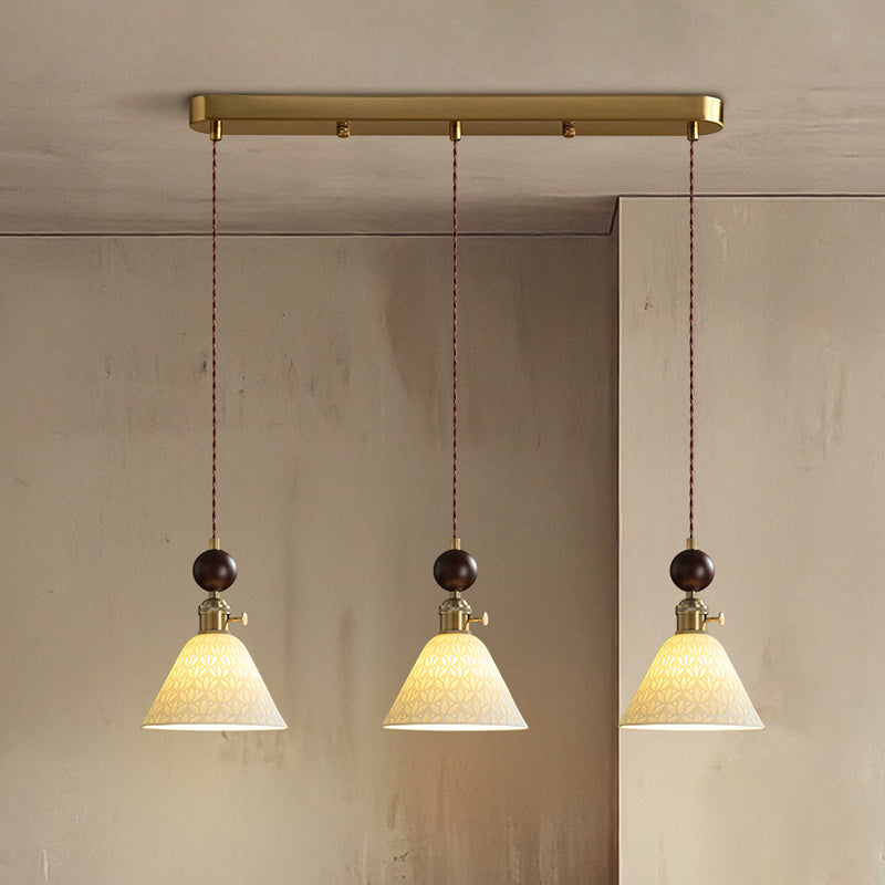 Three cone-shaped ceramic Clérachic pendants with round walnut tops, lit and hung from a brass bar canopy.