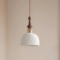 A white ceramic Clérachic pendant with a rose pattern in relief, unlit, against a peach-toned wall.