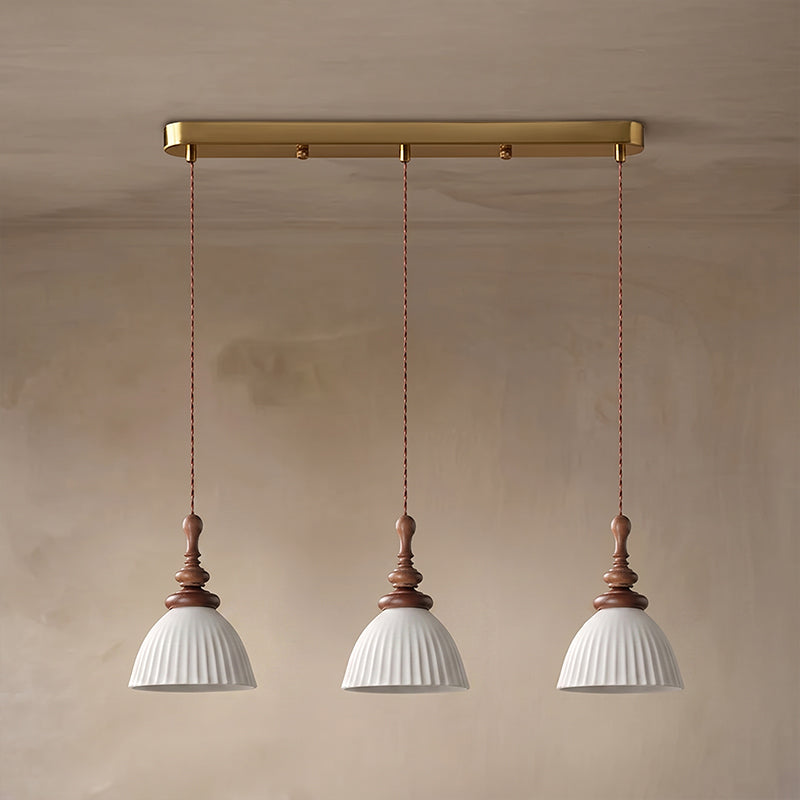 Three white ribbed ceramic Clérachic pendants hung from a brass bar canopy on twisted cords, against a plaster wall.