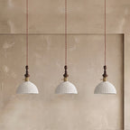 Three white ribbed ceramic Clérachic pendants with brass switch collars, hung in a row against a plaster alcove.