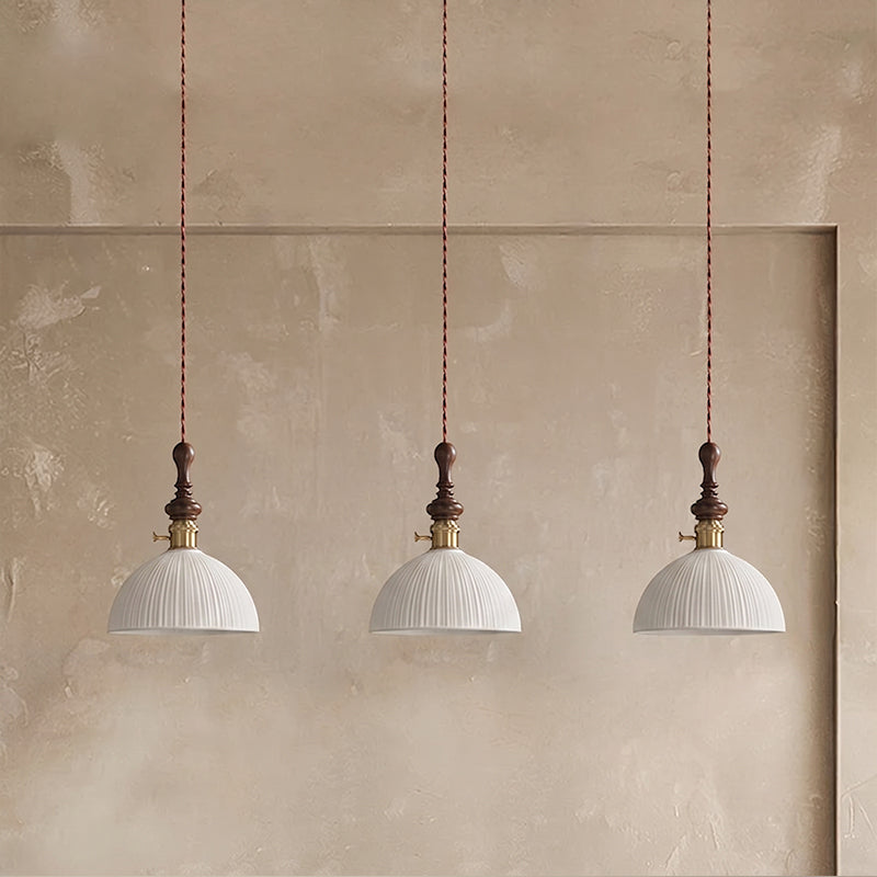 Three white ribbed ceramic Clérachic pendants with brass switch collars, hung in a row against a plaster alcove.