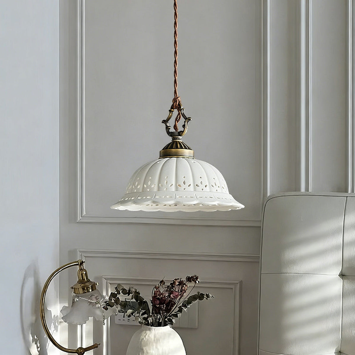 A Clérachic pendant with a pierced white dome hangs against a panelled grey wall, with a white sofa and a vase of dried flowers.