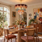The Clérachic ceramic chandelier lit above a round wooden dining table with cane chairs, in a room with arched windows and bold art.