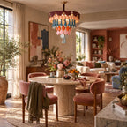 A Clérachic ceramic chandelier glows above a round stone-topped table with rose velvet chairs and a green throw, in an open-plan room.