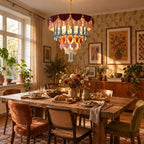 A lit Clérachic chandelier hangs above a rustic table laid for a meal, with rust, olive and cane chairs and framed floral art behind.