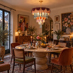 The Clérachic chandelier glows above a round stone dining table set with candles, with velvet and cane chairs and tall windows.
