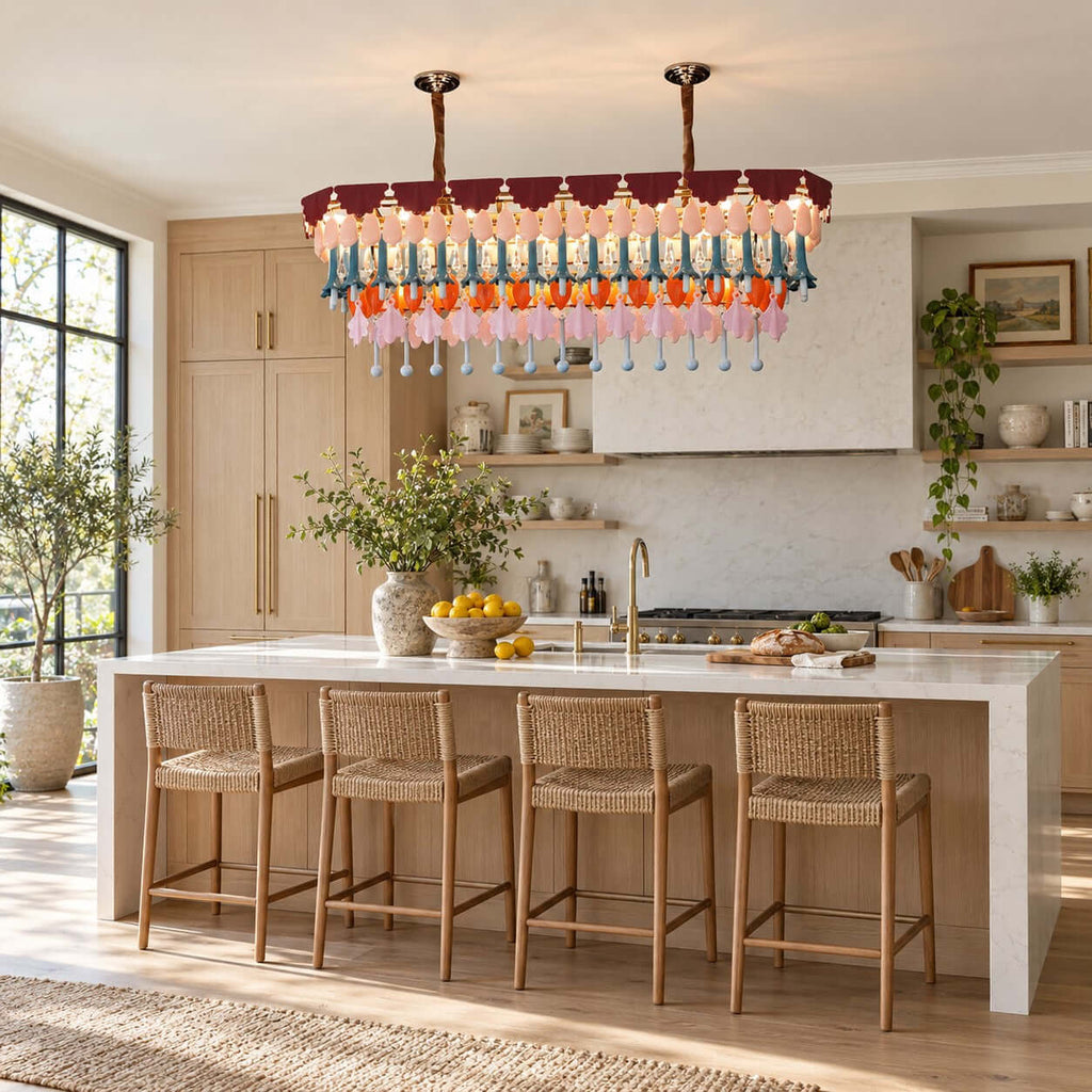 A rectangular Clérachic chandelier on two chains above a stone-topped kitchen island with four woven bar stools and warm light.